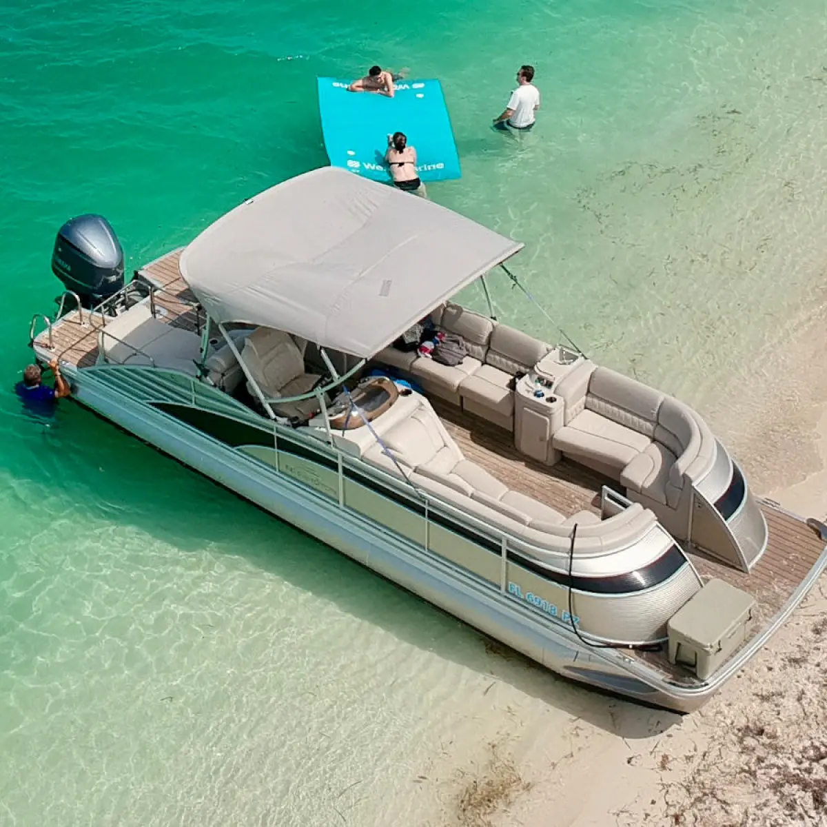 Pontoon boat on turquoise water near sandy beach, two people on a float.