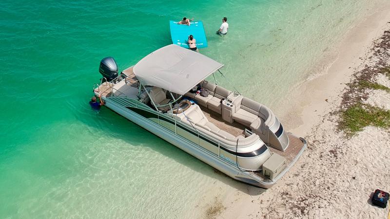 Pontoon boat on turquoise water near sandy beach, two people on a float.