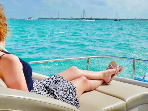 Person relaxing on a boat in the ocean, facing the horizon with sailboats in the distance.