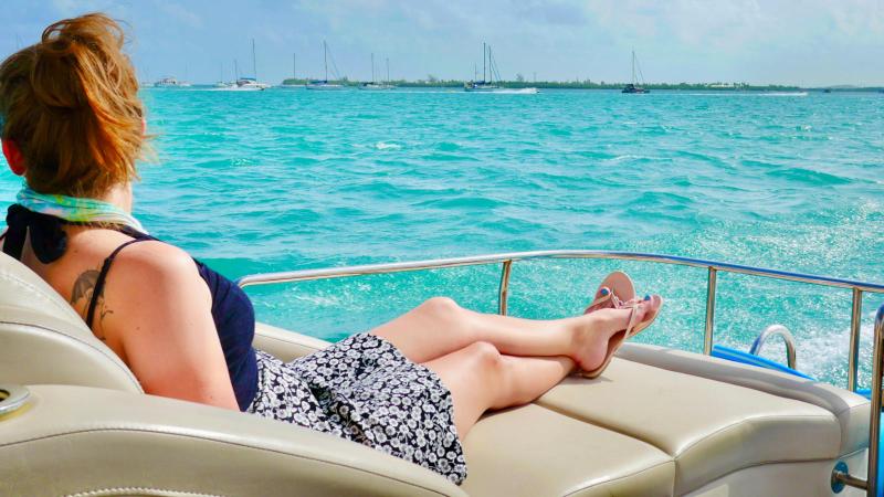 Person relaxing on a boat in the ocean, facing the horizon with sailboats in the distance.