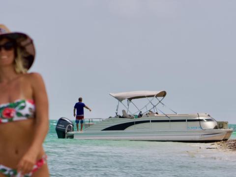 Woman in floral bikini and hat on beach, boat in background on water.