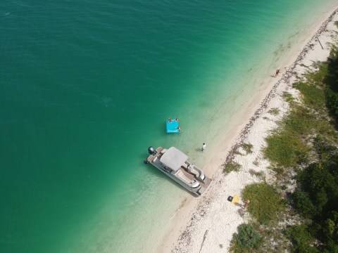 Aerial view of a motorboat and people lounging on a float near a sandy beach with turquoise water.