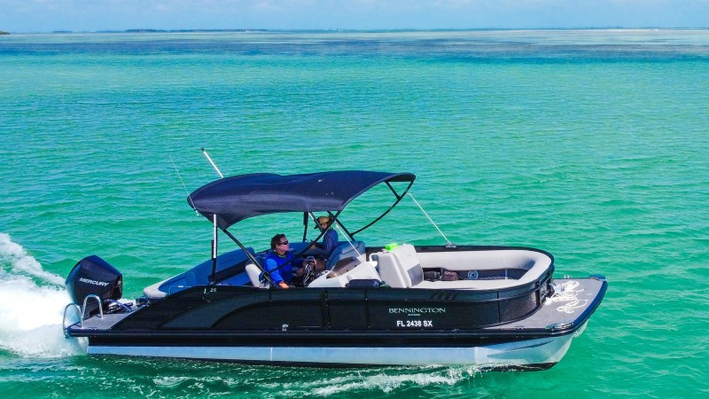 Small motorboat with canopy cruising on clear turquoise water under blue sky.