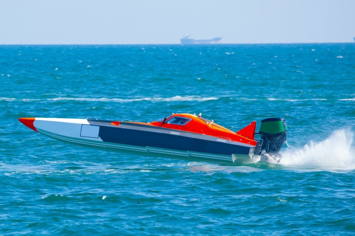 Orange speedboat racing on the ocean, leaving a trail of water spray.