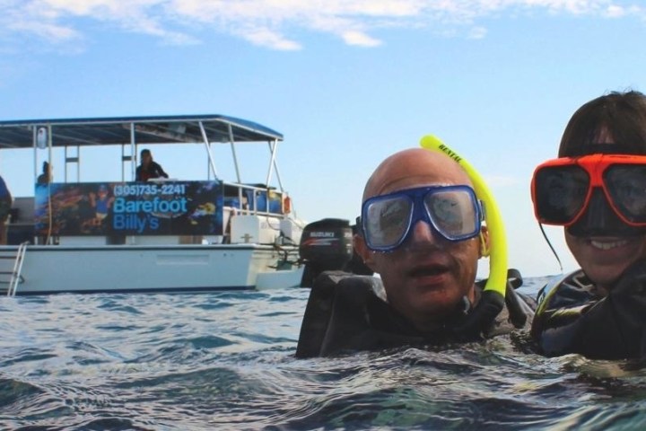 Two snorkelers in water near a boat with a banner and people onboard.