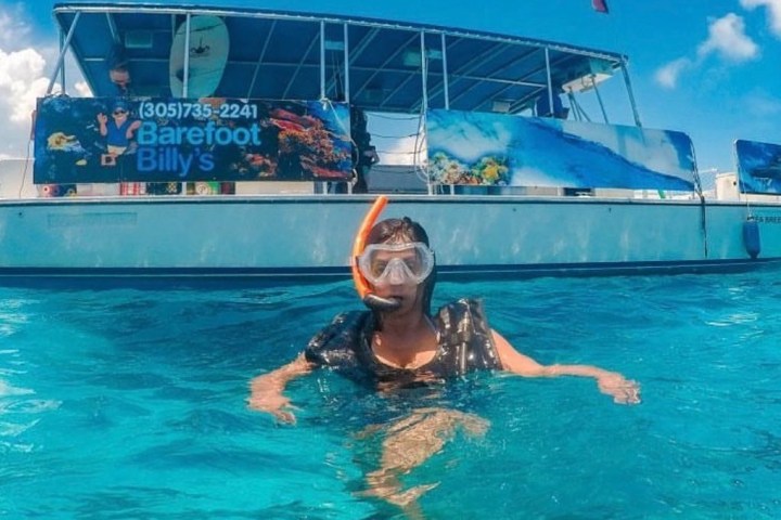 Person snorkeling near a boat in clear blue water.