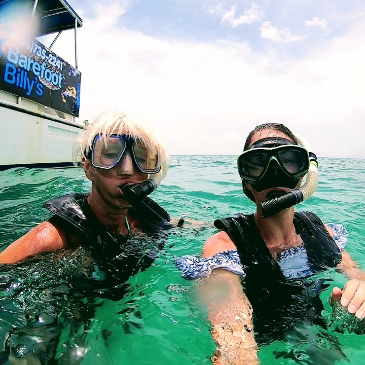 Two snorkelers in masks near a boat on a sunny day.
