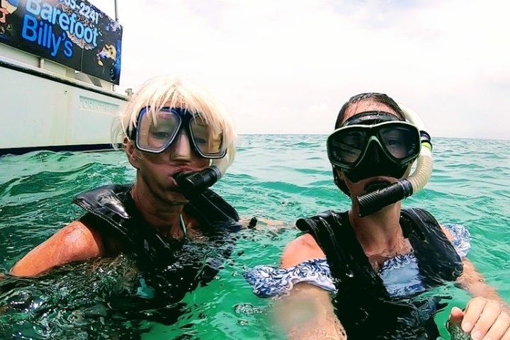 Two snorkelers in masks near a boat on a sunny day.