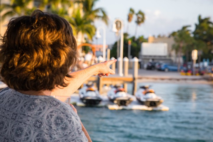 Person pointing at docked jet skis on a sunny waterfront.