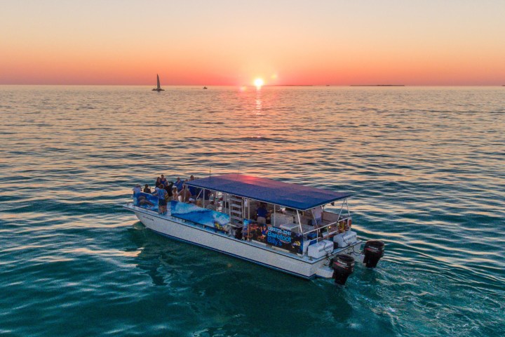 Boat on ocean at sunset with sailboat in distance.