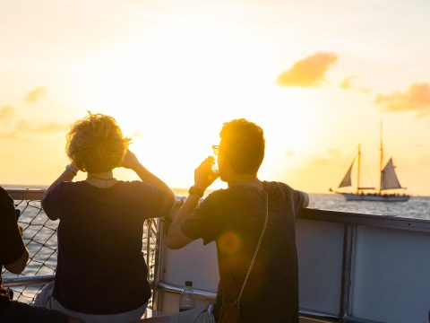 People on boat at sunset, distant sailboat on horizon.