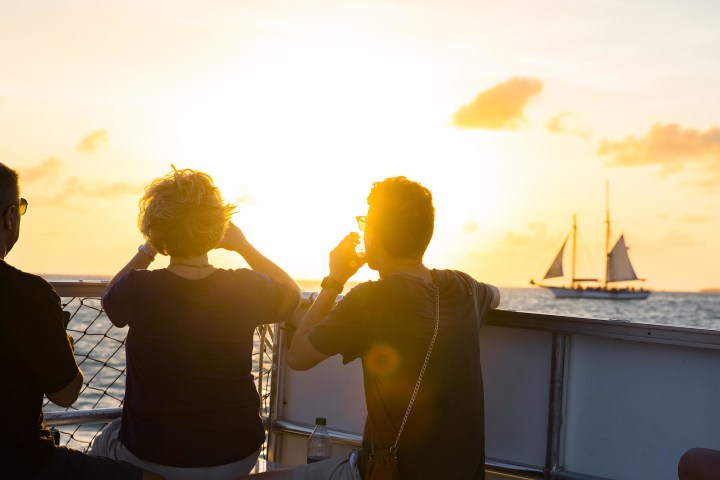 People on boat at sunset, distant sailboat on horizon.