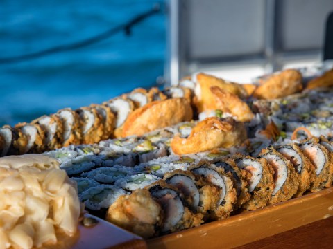Assorted sushi on a wooden tray with ocean in the background.