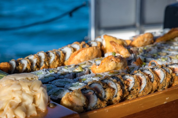 Assorted sushi on a wooden tray with ocean in the background.