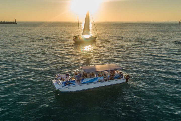 Boats on ocean at sunset with sun reflecting on water.