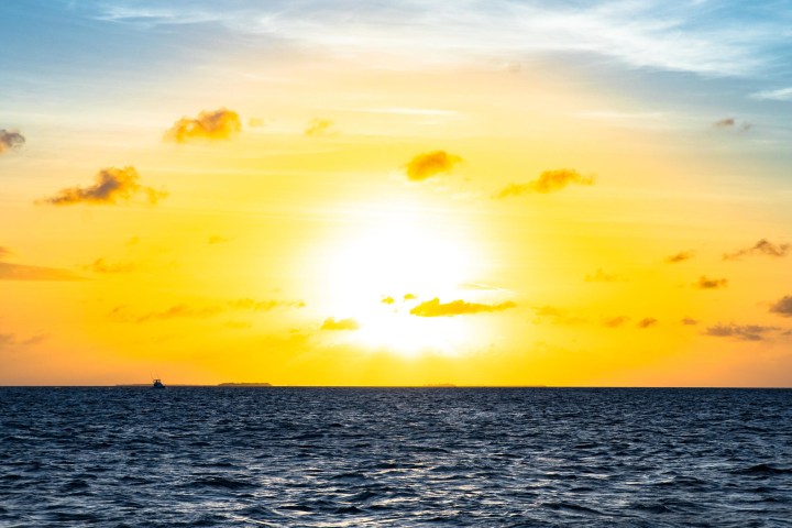 Sunset over ocean with bright orange sky and scattered clouds.