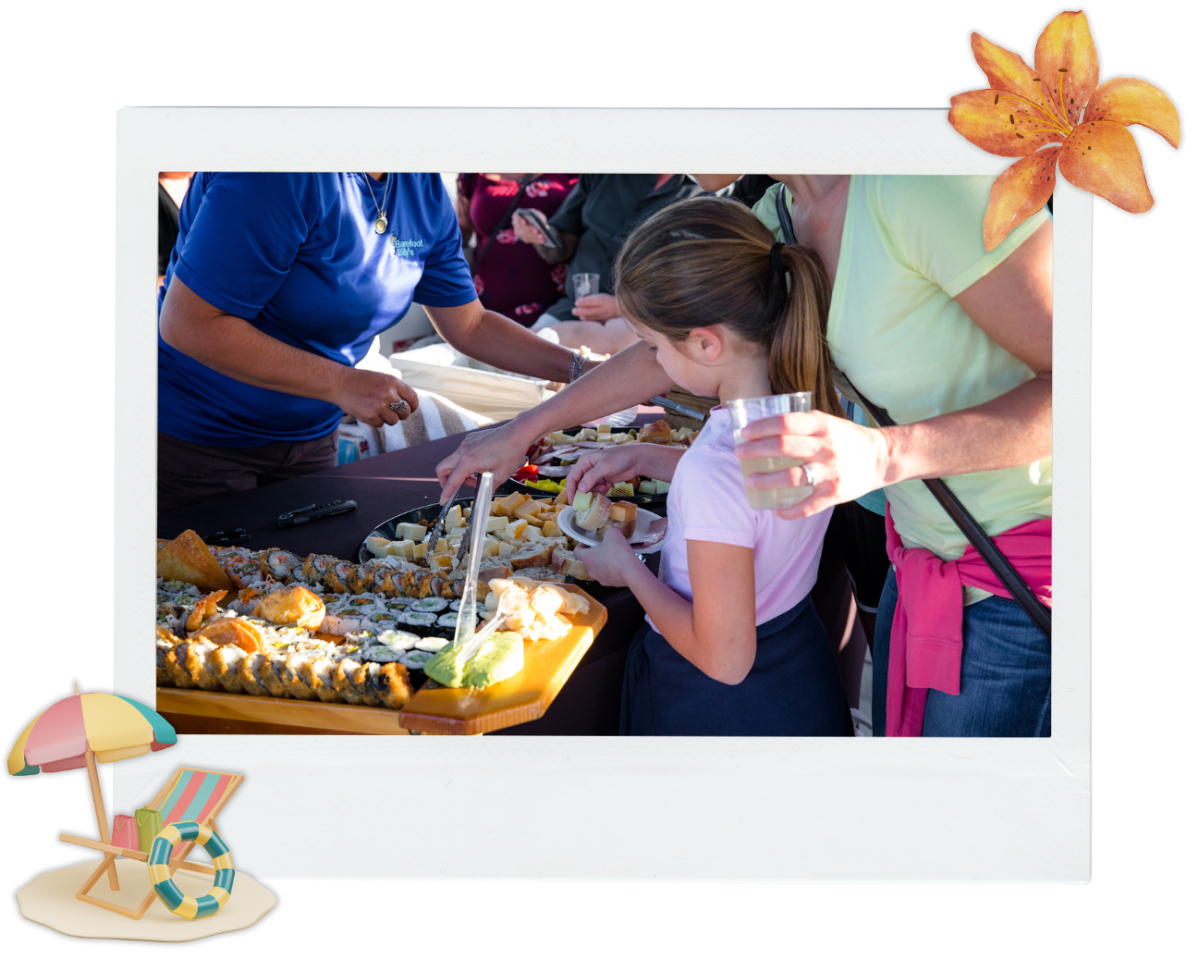 People serving food at an outdoor buffet table with summer decor.