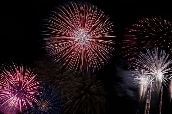 Vibrant red, pink, and white fireworks against a dark sky.